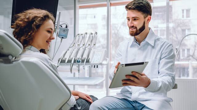 Dentista mostrando um tablet para uma paciente no consultório odontológico