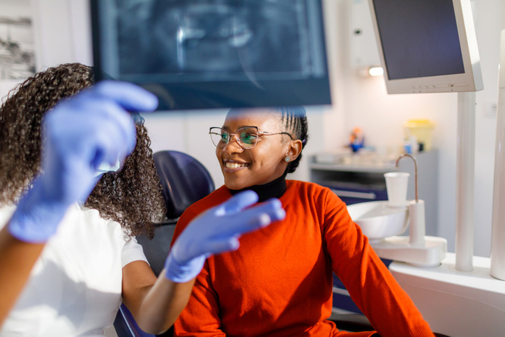 Paciente sorri enquanto o dentista analisa radiografia, explicando os cuidados necessários antes de extrair o siso em consultório odontológico.