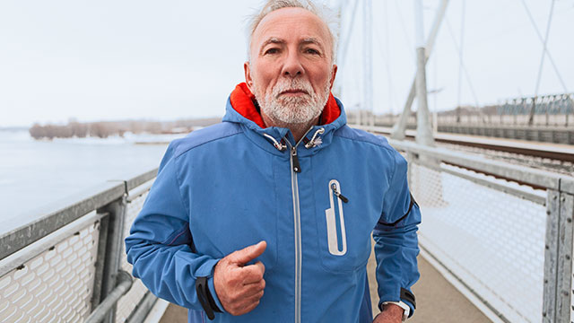 Um homem sênior de casaco azul correndo na ponte