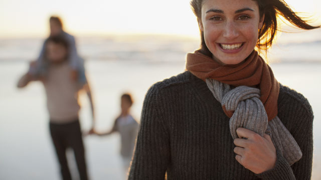 mulher sorrindo sem cárie na praia com o marido e os filhos atrás
