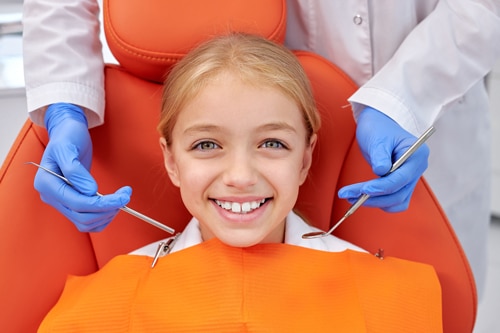 Menina sorrindo na cadeira do dentista durante exame para prevenção de cárie.