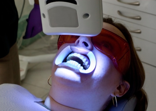 Paciente em consultório odontológico usando proteção ocular durante aplicação de luz azul no procedimento de colocação de facetas de resina.