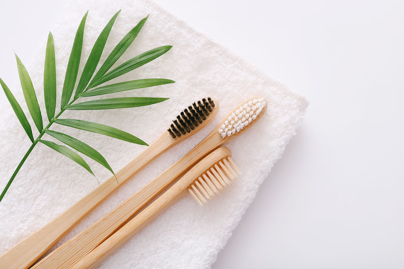 Escovas de dentes de bambu sobre toalha branca, acompanhadas de folha verde, representando o uso de produtos veganos.