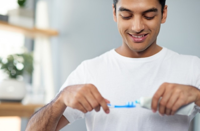 Homem sorrindo enquanto coloca a melhor pasta de dente na escova para escovar os dentes