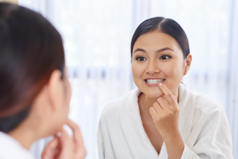 Mulher observando seus dentes limpos no espelho após usar um enxaguante bucal 