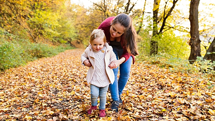 Mãe e filha andando em trilha com folhas de outono no chão