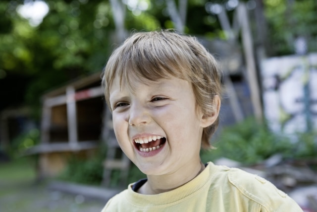 Criança sorrindo no jardim com árvore ao fundo