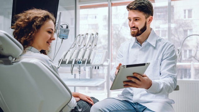 Dentista mostrando um tablet para uma paciente no consultório odontológico