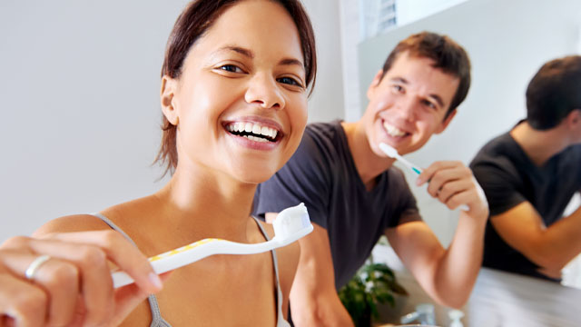 Mulher praticando cuidados com os dentes ao lado do marido 