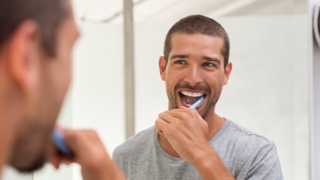 Homem escovando os dentes com escova macia e Creme Dental Colgate Total Original Mint para prevenir o biofilme dental.