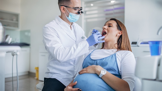 Mulher em consulta odontológica, recebendo atenção para tirar dúvida se grávida pode fazer clareamento dental.