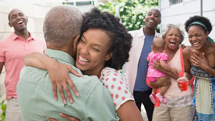 Mulher sorridente abrançando parente observada por outros parentes