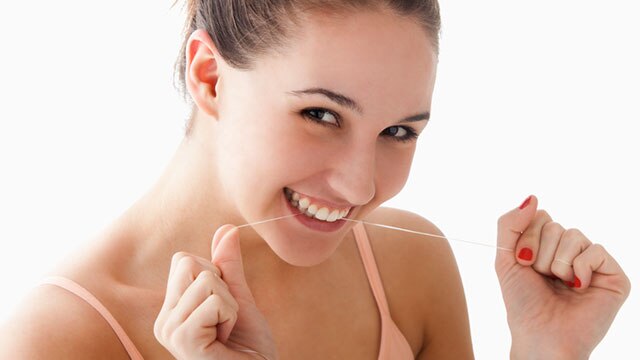 Mulher limpando os dentes com fio dental