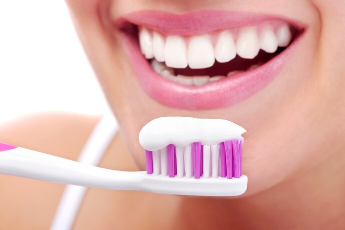 Pessoa sorridente segurando uma escova de dentes com creme dental com flúor, pronta para escovar os dentes