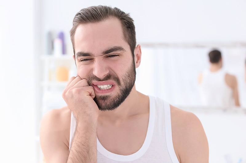 Homem com mão na bochecha sentindo dor de dente