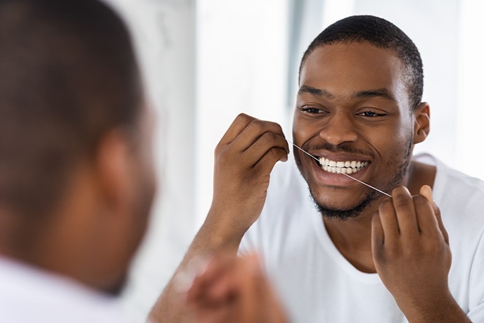 Homem passando fio dental em frente ao espelho