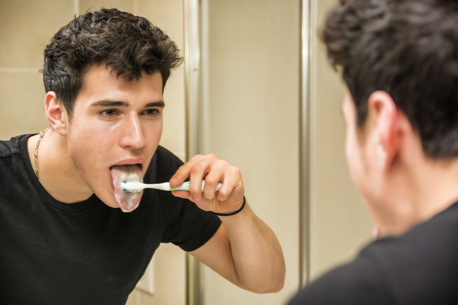 jovem escovando os dentes e limpando a língua com escova de dentes