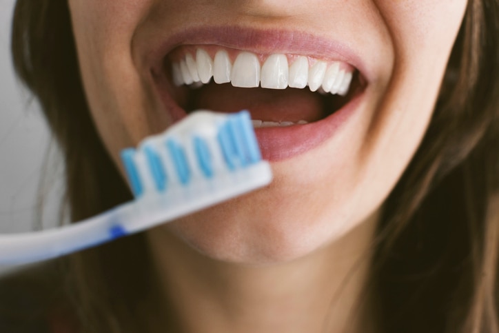 Mulher sorrindo enquanto segura uma escova com creme dental clareador, mostrando dentes brancos e saudáveis em destaque.