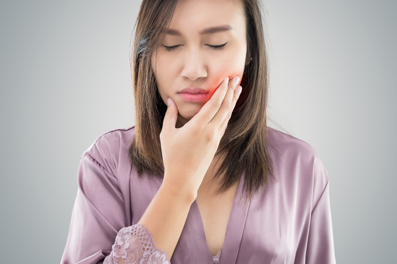 Mulher com a mão na bochecha sentindo incômodo após extração de dentes.