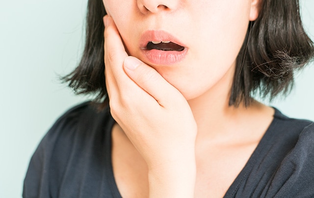 Foco em uma mulher com a boca entreaberta, levando a mão à bochecha para representar a dor causada pela infecção no dente.