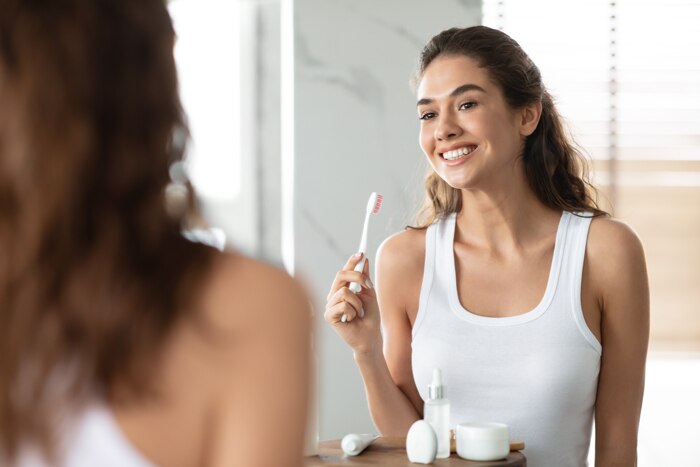 Mulher sorridente em frente ao espelho, segurando uma escova de dentes com o melhor creme dental para tártaro.