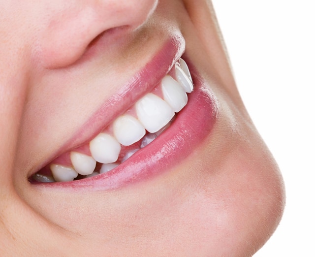Mulher de óculo rosa e olhos fechados, feliz e sorrindo mostrando suas gengivas saudáveis