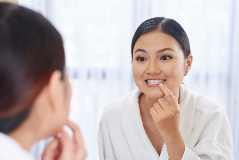 Mulher observando seus dentes limpos no espelho após usar um enxaguante bucal 