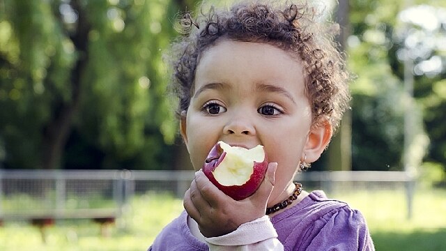 Menino em um parque comendo uma maçã