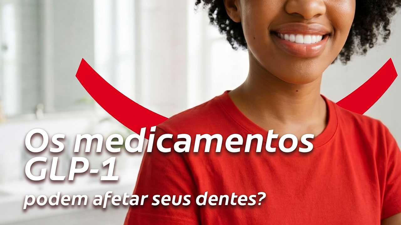 Uma mulher sorridente, com cabelos escuros e cacheados e uma camiseta vermelha, em pé em um banheiro todo branco.