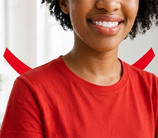 Uma mulher sorridente, com cabelos escuros e cacheados e uma camiseta vermelha, em pé em um banheiro todo branco.