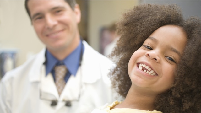 Mulher jovem sorrindo ao lado de um dentista de jaleco branco em um ambiente clínico, com foco no rosto e clima acolhedor de atendimento.