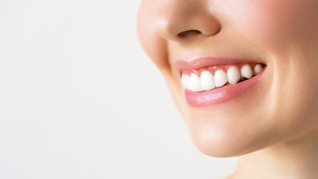 Close-up do sorriso de uma pessoa com dentes alinhados e lábios com tom rosado, em fundo claro, destacando higiene bucal e saúde dental