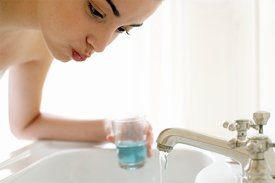 Mulher fazendo bochecho com enxaguante bucal PerioGard para cuidar da saúde da gengiva antes de uma cirurgia plástica facial.