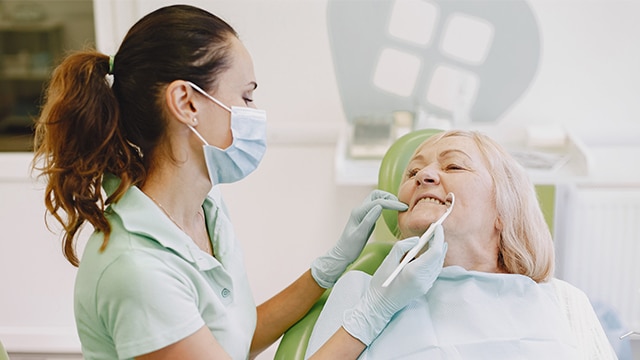 Dentista atenciosa examina paciente idosa sorridente no consultório enquanto esclarece a dúvida se o implante dentário dói.