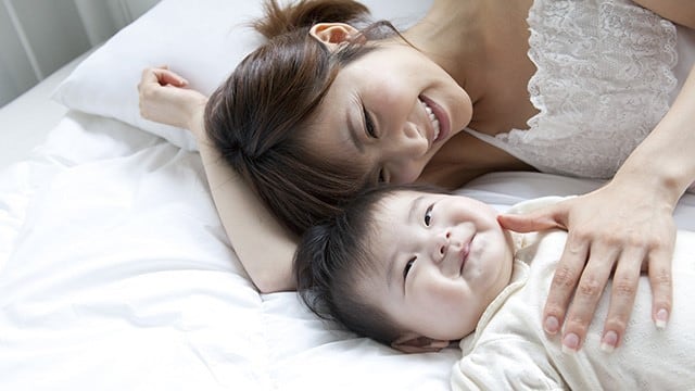 Mãe e bebê deitadas em uma cama sorrindo