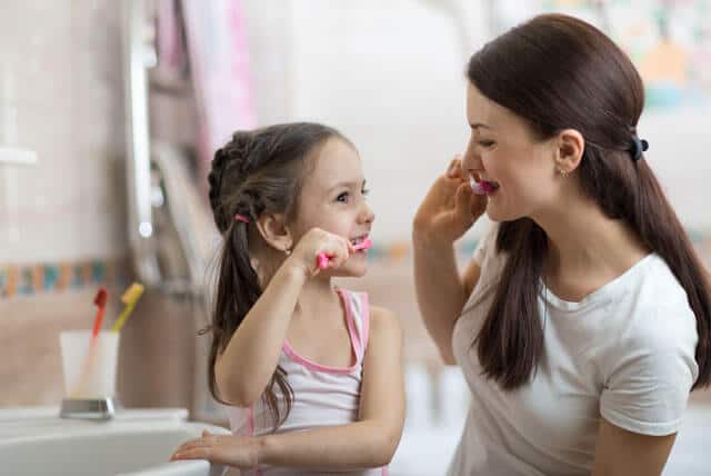 Mulher escovando os dentes com a filha