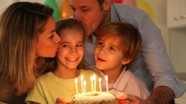 Pais e filhos assoprando a vela de um bolo de aniversário