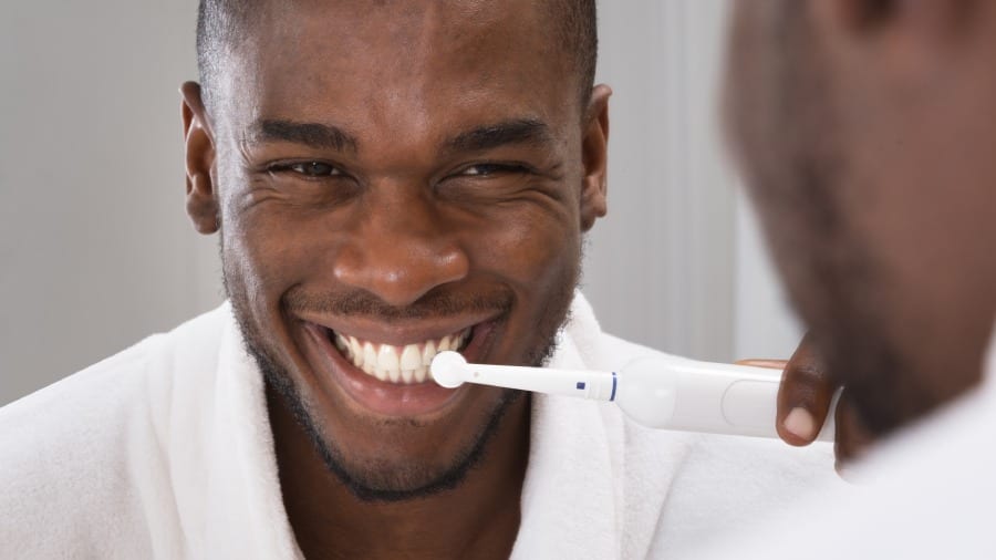 Homem negro escovando os dentes com escova dental elétrica