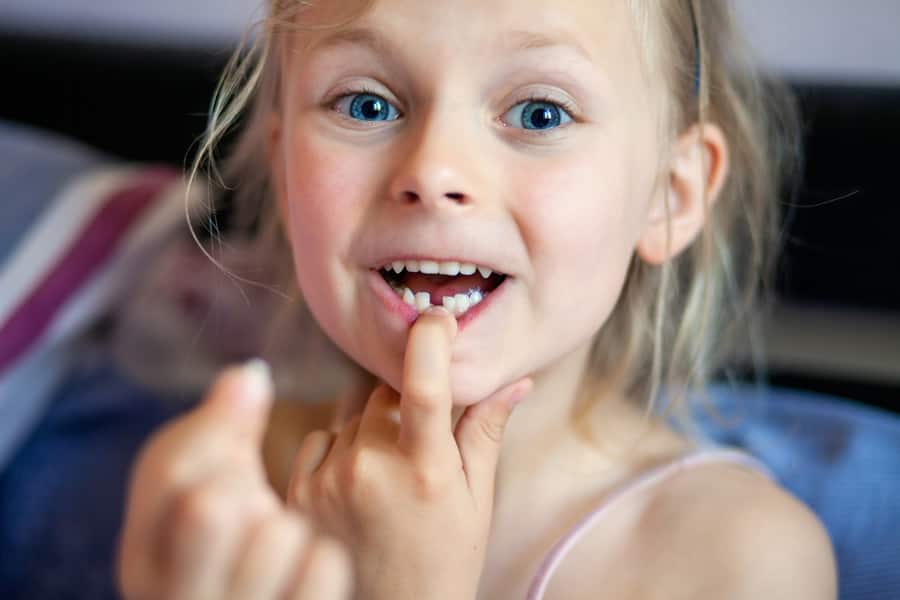 Criança sem dente, mostrando o dentinho que caiu.
