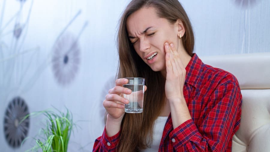 Jovem com dentes sensíveis sente dor com um copo de água na mão