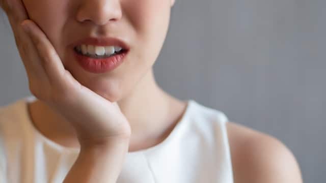 Foto próxima ao rosto de uma mulher, com a mão na bochecha por causa de uma dor de dente