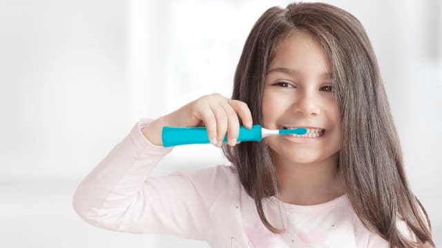 Menina escovando os dentes com uma escova de dente elétrica