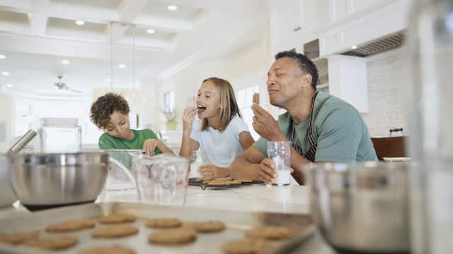 um homem de idade avançada, um menino e uma menina sentados à mesa consumindo biscoitos.