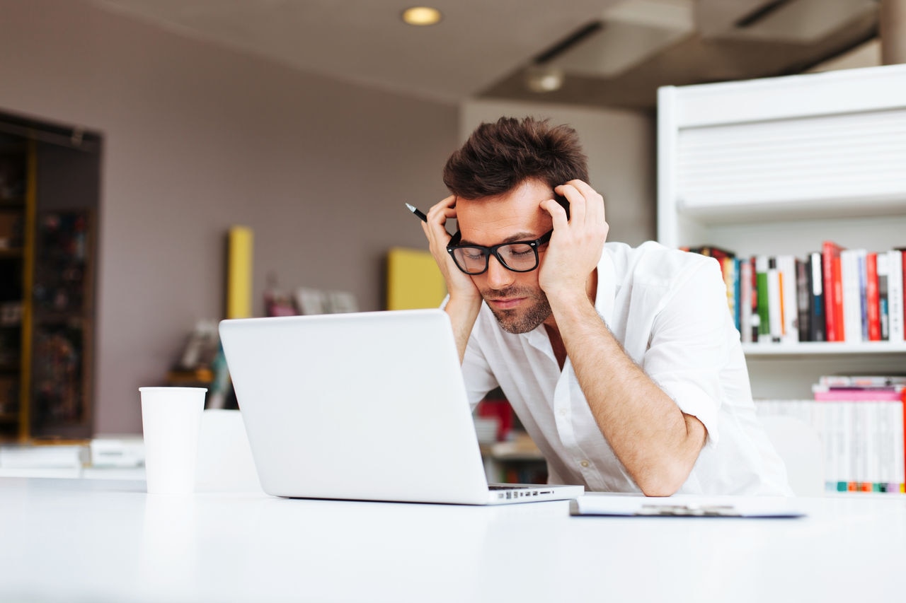Homem com expressão cansada olhando para o laptop, representando fadiga constante, que pode ser um dos sintomas de diabetes