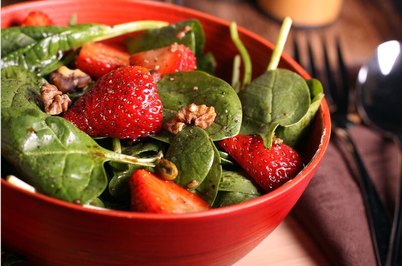 Salada fresca com espinafre, morangos e nozes em uma tigela vermelha, representando uma combinação de alimentos saudáveis e nutritivos