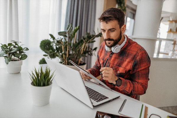 Homem participando de uma entrevista de emprego online, usando laptop e tablet em um ambiente organizado e tranquilo 