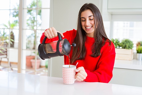 Mulher sorridente preparando uma xícara de café cremoso com uma cafeteira francesa. 