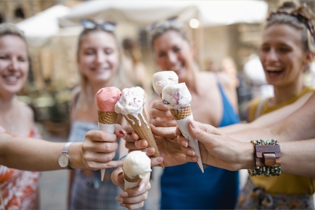 Grupo de quatro amigas em círculo segurando casquinhas de sorvete italiano ao centro