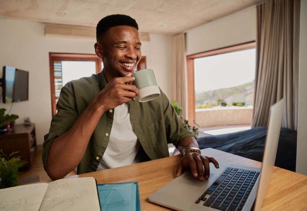 rapaz sorrindo enquanto toma um dos tipos de café e usa seu laptop